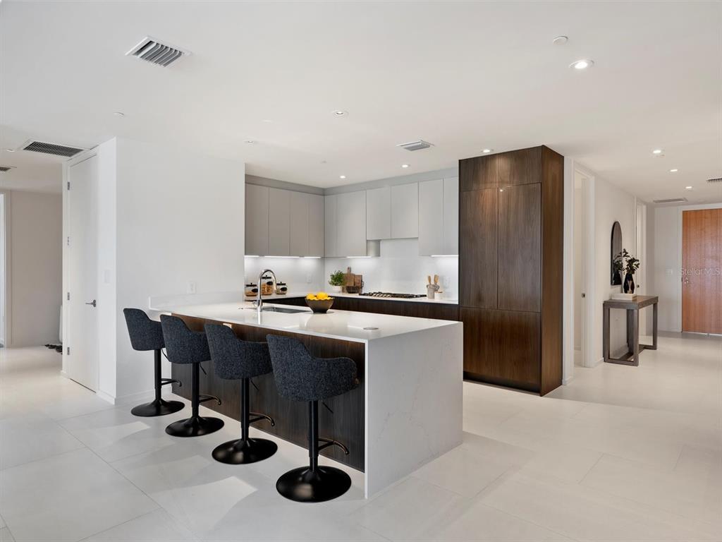 A modern multi-story apartment building overlooks a swimming pool with lounge chairs and palm trees — 1020 SUNSET POINT ROAD UNIT 103, CLEARWATER, FL
