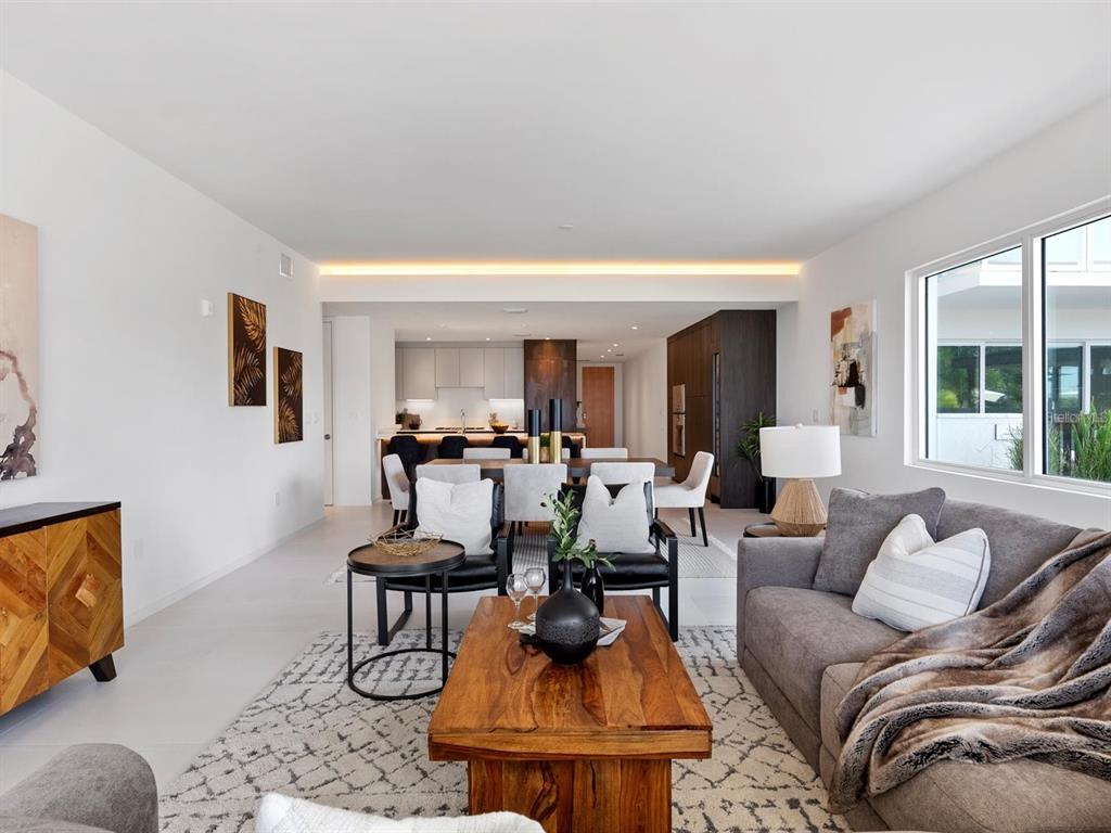 A modern, open-concept dining and living area features a dark wood table and water views — 1020 SUNSET POINT ROAD UNIT 103, CLEARWATER, FL