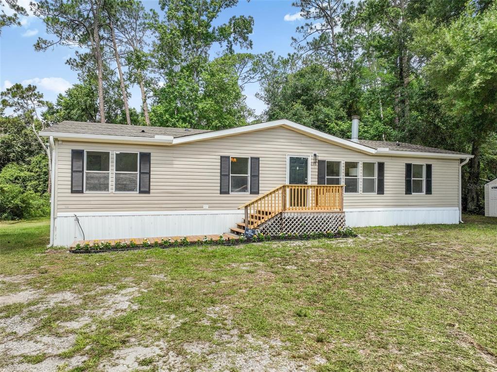 A single-story manufactured home with beige siding and a wooden front porch sits on grass — 2318 COCONUT BOULEVARD, BUNNELL, FL