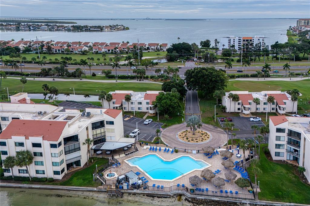 An aerial view shows a waterfront condominium complex with a swimming pool and parking lot — 5541 PUERTA DEL SOL BOULEVARD S UNIT 116, ST PETERSBURG, FL