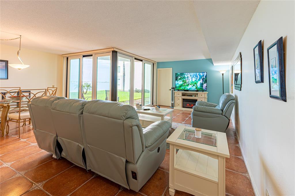 A living room features light-colored leather furniture, tile flooring, and large glass doors overlooking water — 5541 PUERTA DEL SOL BOULEVARD S UNIT 116, ST PETERSBURG, FL