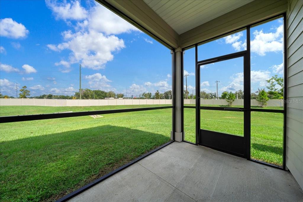 A screened-in concrete patio overlooks a grassy backyard enclosed by a white vinyl fence — 3339 SE 37TH AVENUE ROAD, OCALA, FL