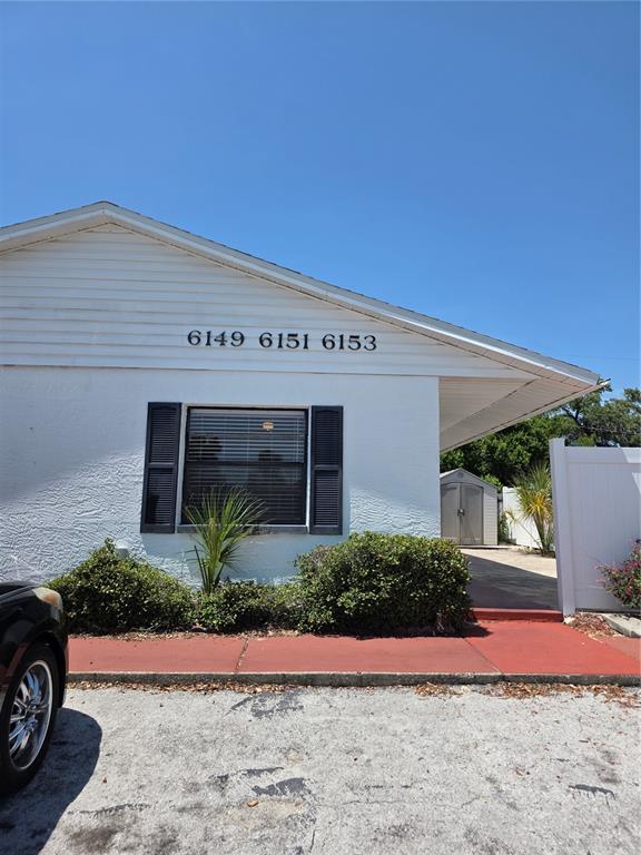 A white building exterior features a window with black shutters and three address numbers — 6153 SAPPHIRE DRIVE, NEW PORT RICHEY, FL