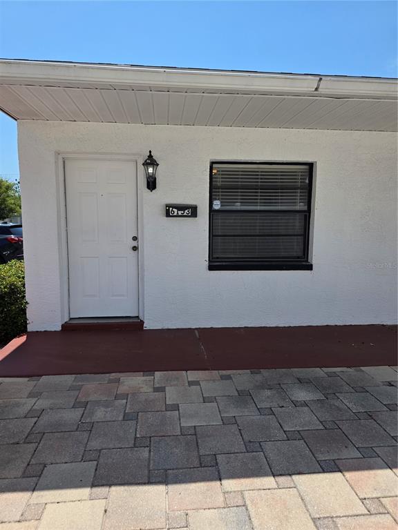 A white exterior wall features a front door, a window, and a paved patio area — 6153 SAPPHIRE DRIVE, NEW PORT RICHEY, FL