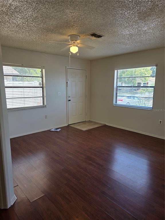 An empty living room features dark wood-look flooring, white walls, two windows, and a ceiling fan — 6153 SAPPHIRE DRIVE, NEW PORT RICHEY, FL
