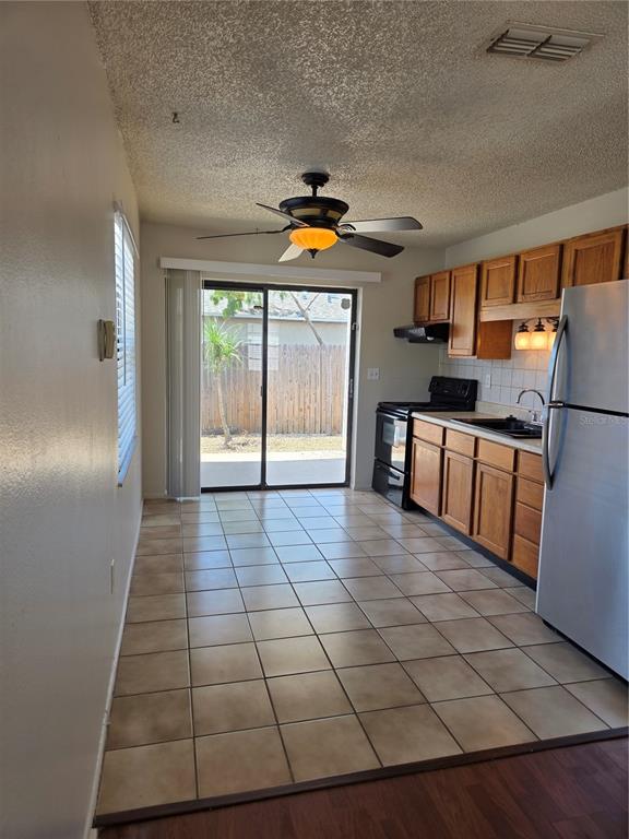 A kitchen with wood cabinets, stainless steel refrigerator, tile flooring, and a sliding glass door — 6153 SAPPHIRE DRIVE, NEW PORT RICHEY, FL