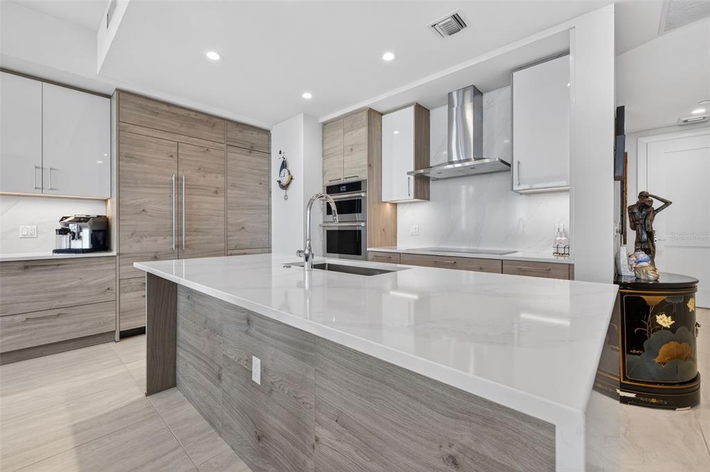 A modern kitchen with wood-toned cabinetry and a white waterfall island overlooks a city view — 301 1ST STREET S UNIT 1505, ST PETERSBURG, FL