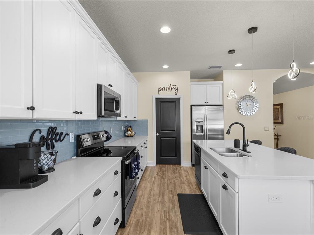 A kitchen features white cabinets, a central island with three stools, and stainless steel appliances — 7117 PARK TREE DRIVE, TAMPA, FL