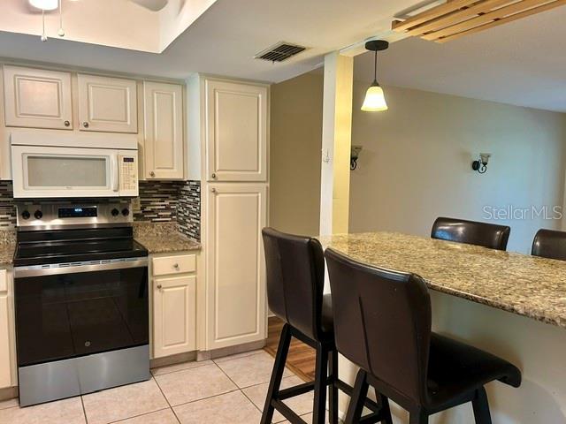 A kitchen features white cabinets, stainless steel appliances, and a granite-topped breakfast bar with stools — 2529 OAKLEAF LANE UNIT 30C, CLEARWATER, FL