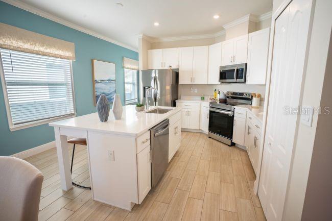 A kitchen with white cabinets, stainless steel appliances, a center island, and light wood-look flooring — 25248 CALUSA DRIVE, PUNTA GORDA, FL