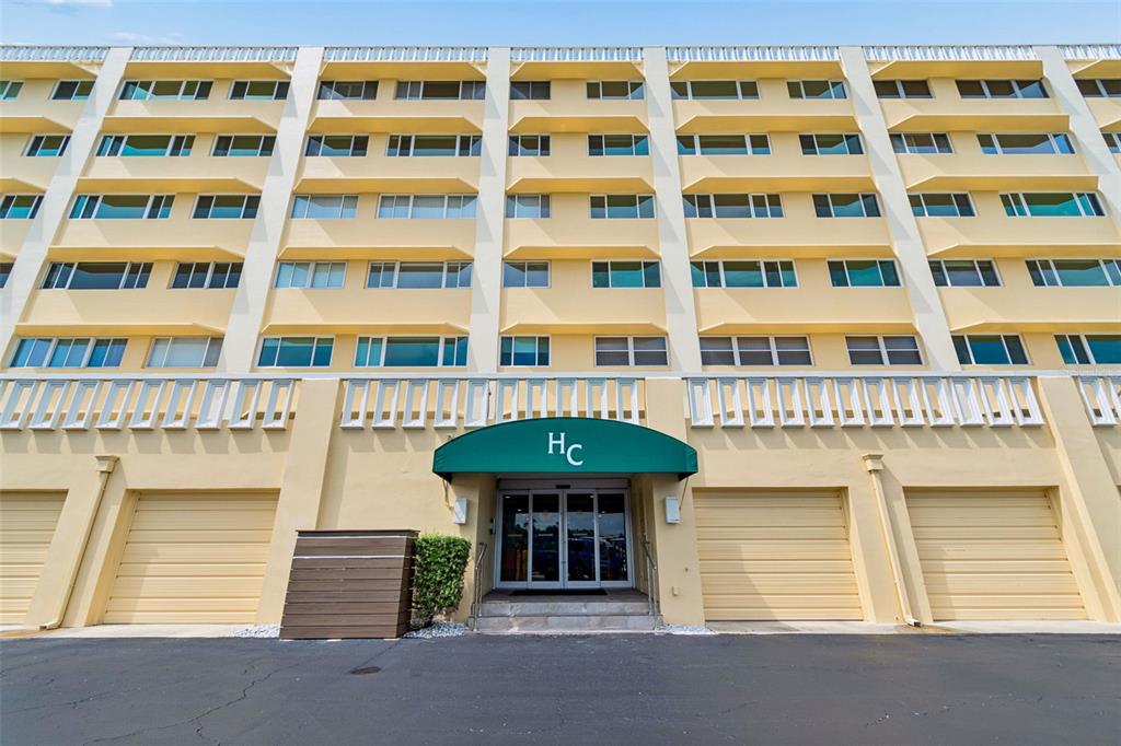 The exterior of a multi-story yellow apartment building features a green entrance awning — 100 BLUFF VIEW DRIVE UNIT 509C, BELLEAIR BLUFFS, FL