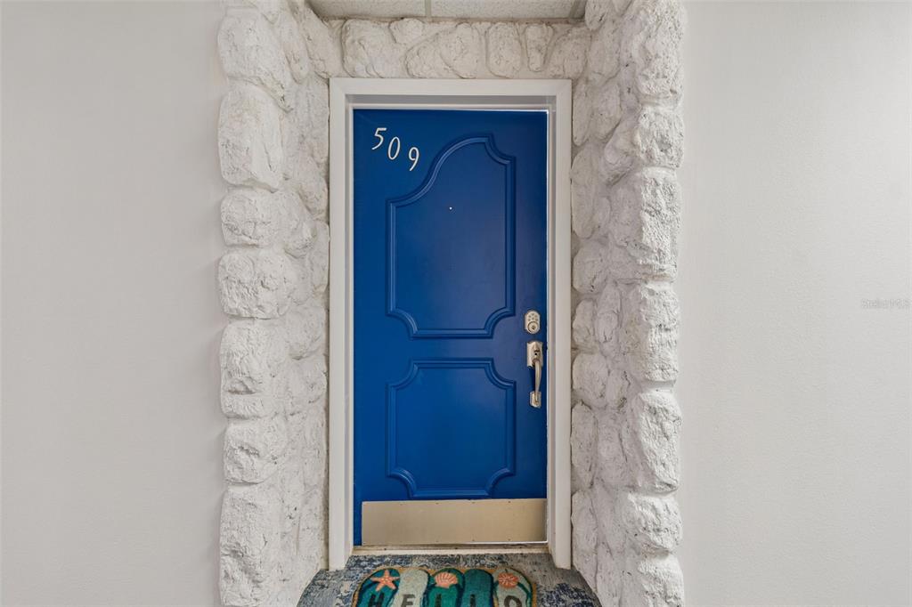 A bright blue front door with the number 509 is framed by white stone masonry — 100 BLUFF VIEW DRIVE UNIT 509C, BELLEAIR BLUFFS, FL
