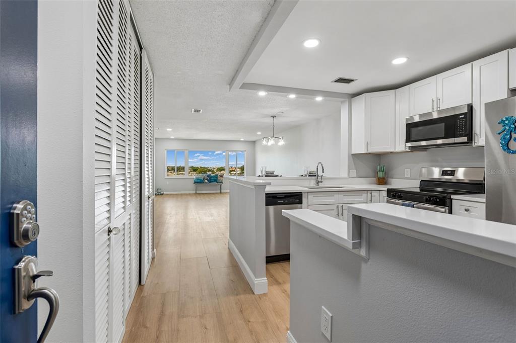 A view from an entryway into a kitchen with white cabinets and a living area — 100 BLUFF VIEW DRIVE UNIT 509C, BELLEAIR BLUFFS, FL