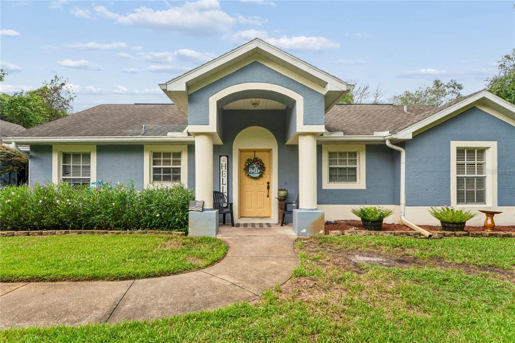 A blue single-story house features a covered entryway with two white columns and a yellow door — 10447 GRANNING LANE, NEW PORT RICHEY, FL