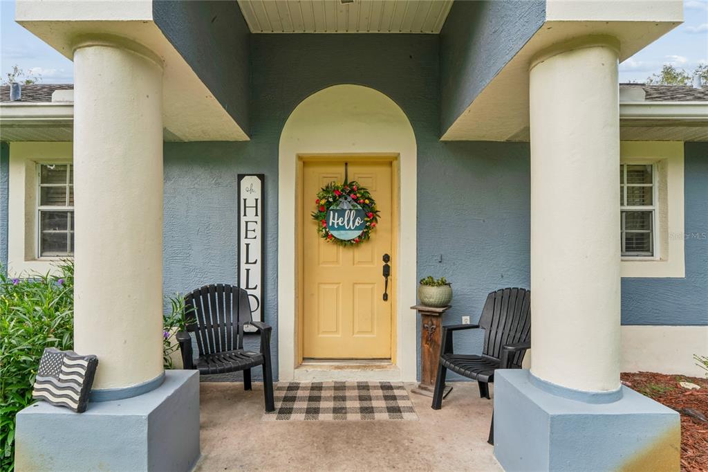 A front porch features two black chairs, a yellow door, and a decorative welcome sign — 10447 GRANNING LANE, NEW PORT RICHEY, FL