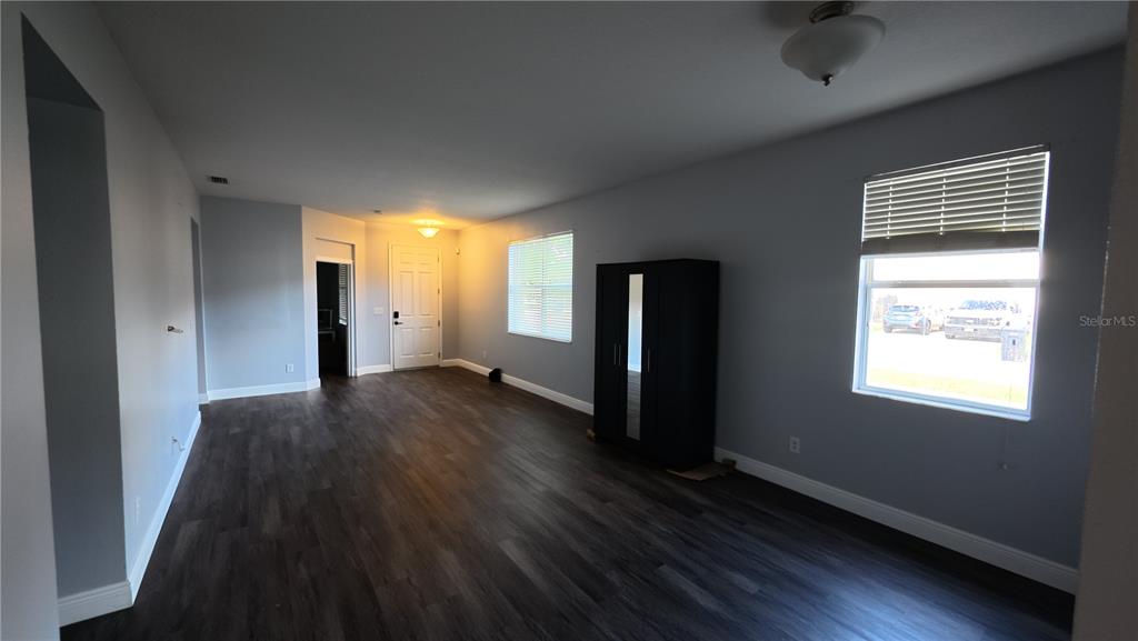 A living room features gray walls, dark wood-look flooring, a black wardrobe, and two windows — 1701 CHALKSAND WAY, RUSKIN, FL