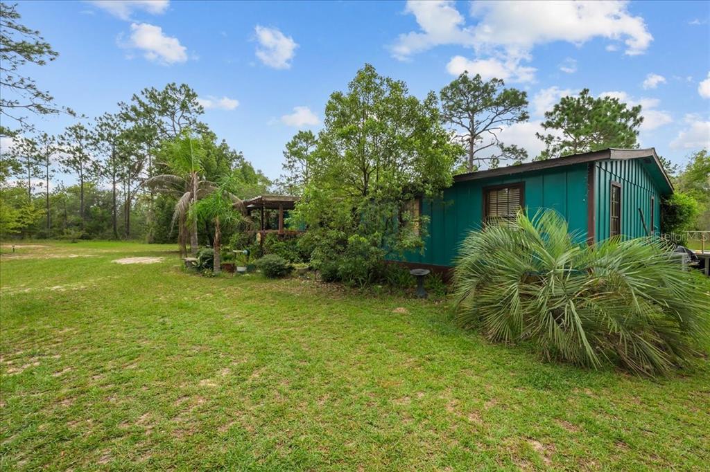 A teal-sided house sits on a grassy lot surrounded by trees and palm plants — 112 BIRCHDALE TRAIL, HAWTHORNE, FL