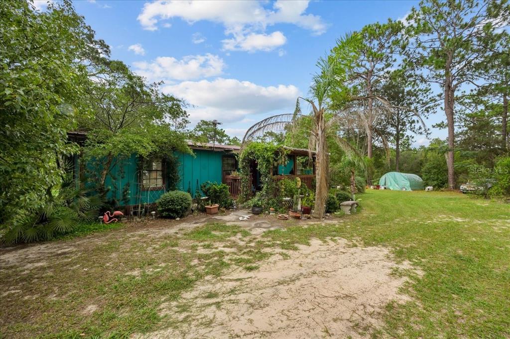 A teal-sided house with a covered porch sits on a sandy lot with trees — 112 BIRCHDALE TRAIL, HAWTHORNE, FL