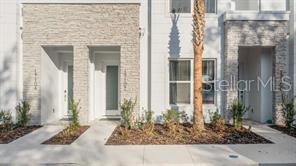 The exterior of two modern townhomes features light stone veneer, white siding, and glass doors — 17102 BLESSING DRIVE, CLERMONT, FL