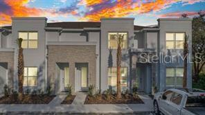 A multi-story townhouse exterior with light gray siding, stone accents, and palm trees — 17102 BLESSING DRIVE, CLERMONT, FL