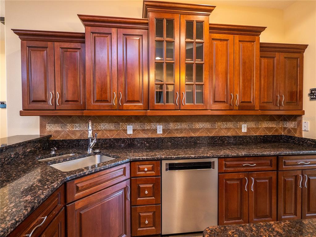 A kitchen features dark wood cabinets, granite countertops, a stainless steel dishwasher, and tiled backsplash — 1719 SW 27TH PLACE, OCALA, FL