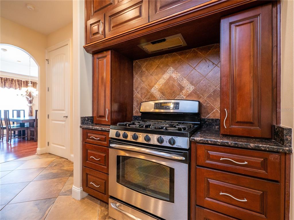 A kitchen features dark wood cabinets, a stainless steel gas range, and a tiled backsplash — 1719 SW 27TH PLACE, OCALA, FL