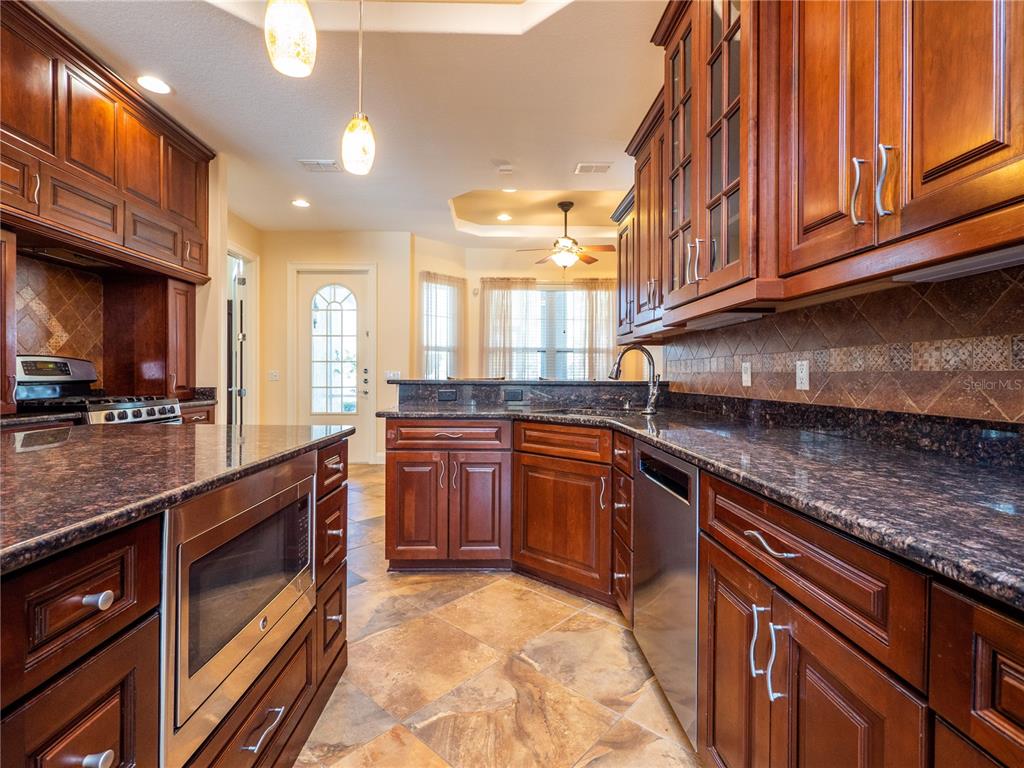 A kitchen features dark wood cabinets, granite countertops, tile flooring, and stainless steel appliances — 1719 SW 27TH PLACE, OCALA, FL