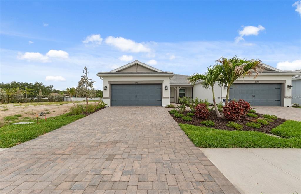 A single-story house with two garage doors and a paved driveway under a blue sky — 1596 TAVIRA PLACE, ENGLEWOOD, FL