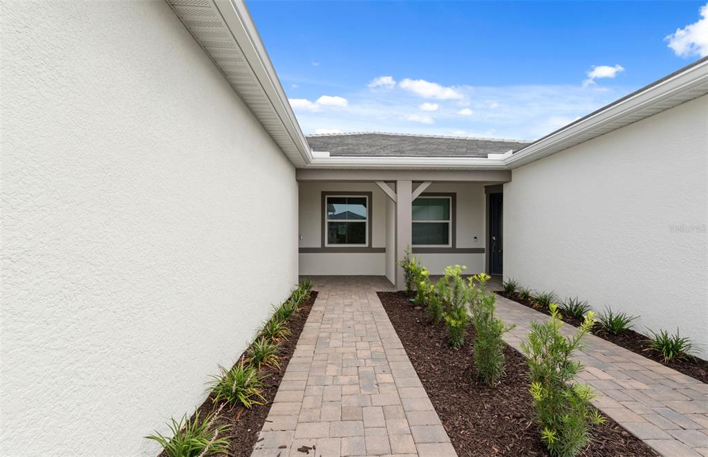 A paved walkway leads to the front entrance of a house with white stucco walls — 1596 TAVIRA PLACE, ENGLEWOOD, FL