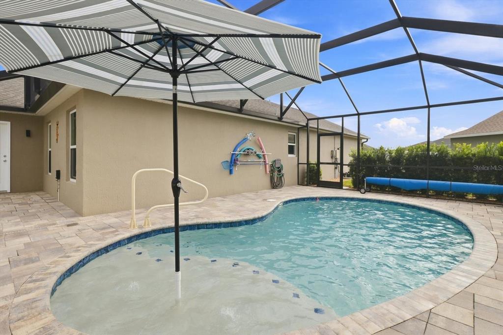 A swimming pool with a striped umbrella sits inside a screened-in patio area — 6088 KECKONEN DRIVE, THE VILLAGES, FL