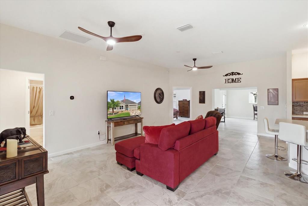 A living room features a red sofa, a television on a console, and tile flooring — 6088 KECKONEN DRIVE, THE VILLAGES, FL