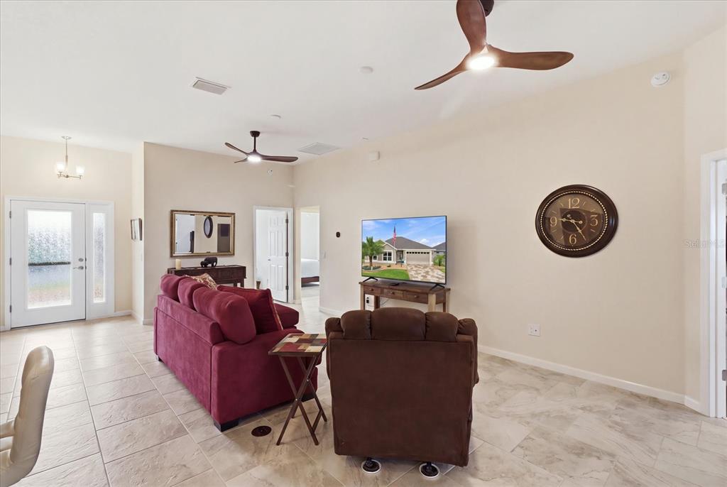 A living room features a red sofa, brown recliner, television, and tile flooring — 6088 KECKONEN DRIVE, THE VILLAGES, FL