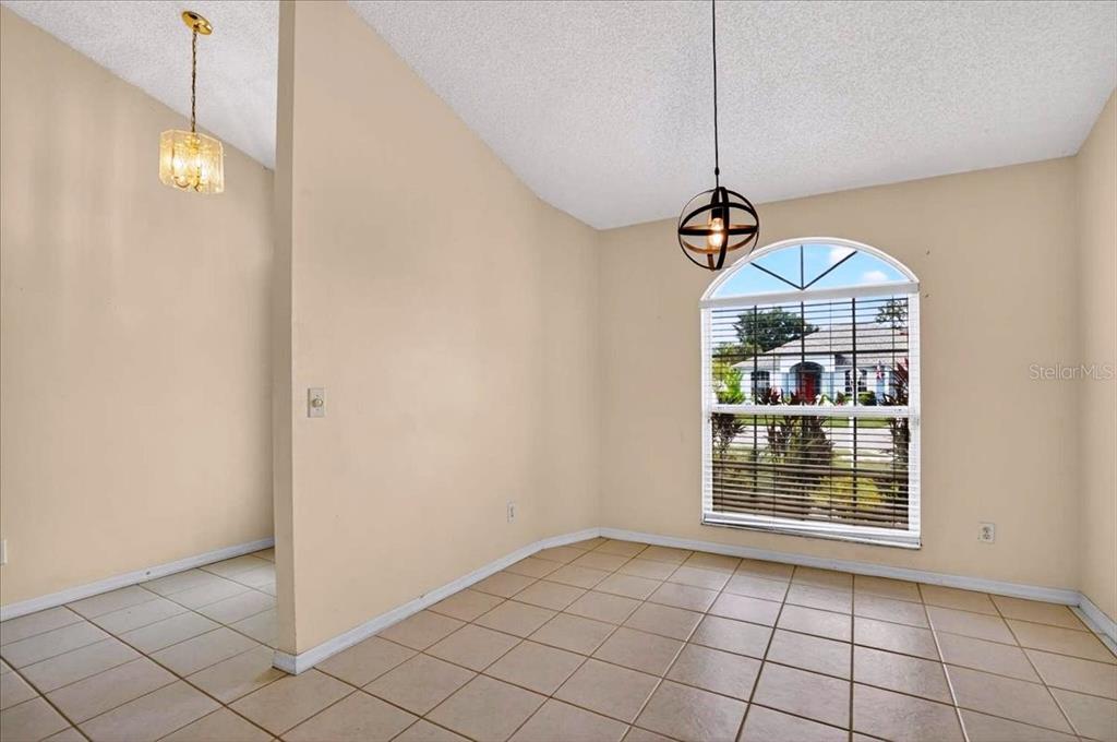 A dining room with beige walls, tile flooring, two light fixtures, and an arched window — 7122 87TH LANE E, PALMETTO, FL
