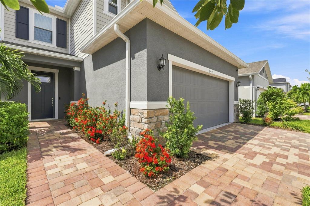 A two-story house exterior features a gray stucco facade, stone accents, and a paved driveway — 11447 GALLATIN TRAIL, PARRISH, FL