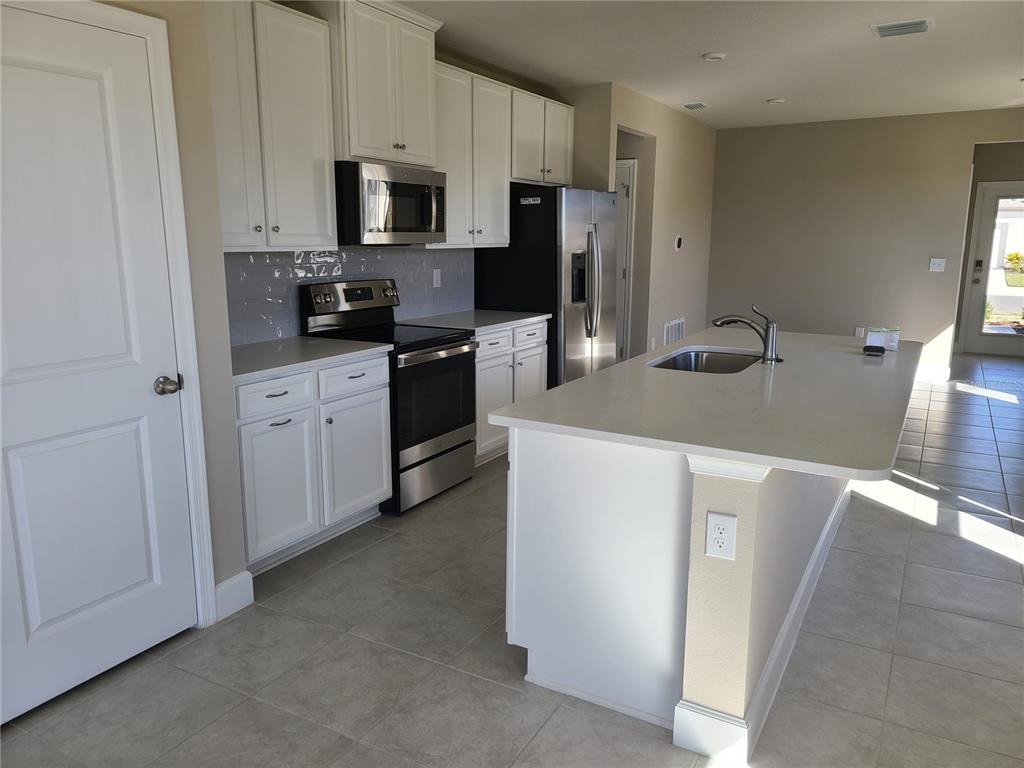A kitchen features white cabinets, stainless steel appliances, a quartz island, and tile flooring — 10013 DAYBREAK GLEN, PARRISH, FL