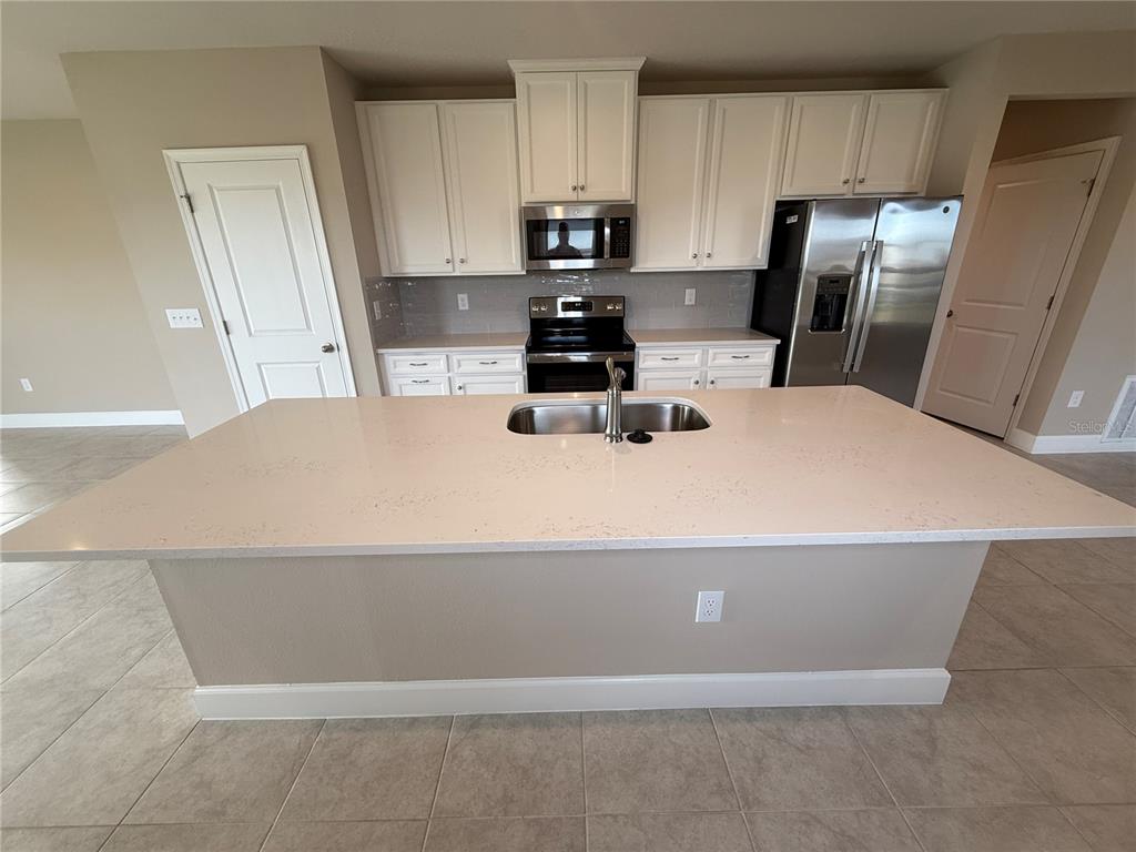 A kitchen features white cabinets, stainless steel appliances, a large island, and light-colored tile flooring — 10013 DAYBREAK GLEN, PARRISH, FL