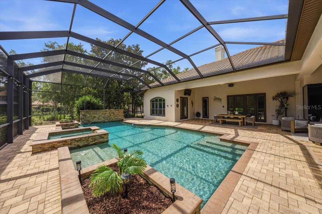 A screened-in patio features a swimming pool with a hot tub and stone accents — 16303 DUNLINDALE DRIVE, LITHIA, FL