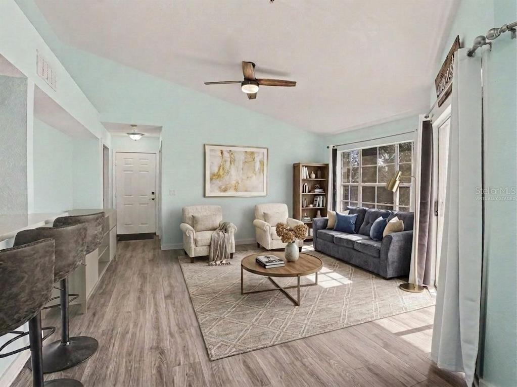 A living room with light blue walls, wood-look flooring, a ceiling fan, and a sofa — 5144 CITY STREET UNIT 233, ORLANDO, FL