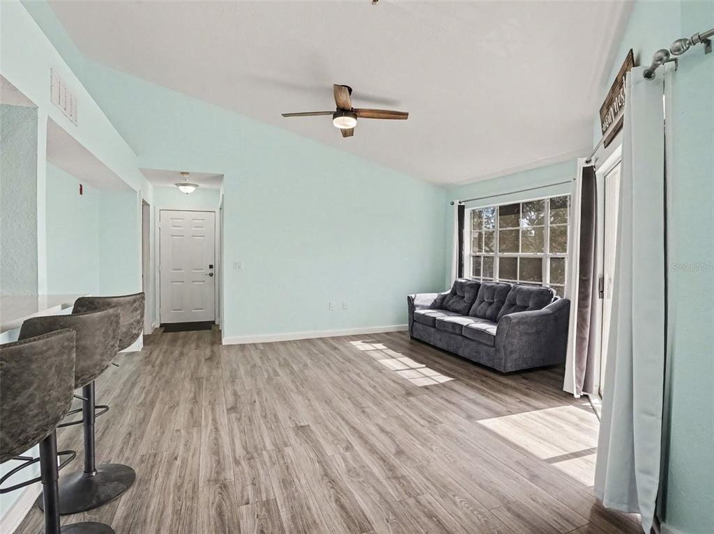 A living room with light blue walls, wood-look flooring, a ceiling fan, and a sofa — 5144 CITY STREET UNIT 233, ORLANDO, FL