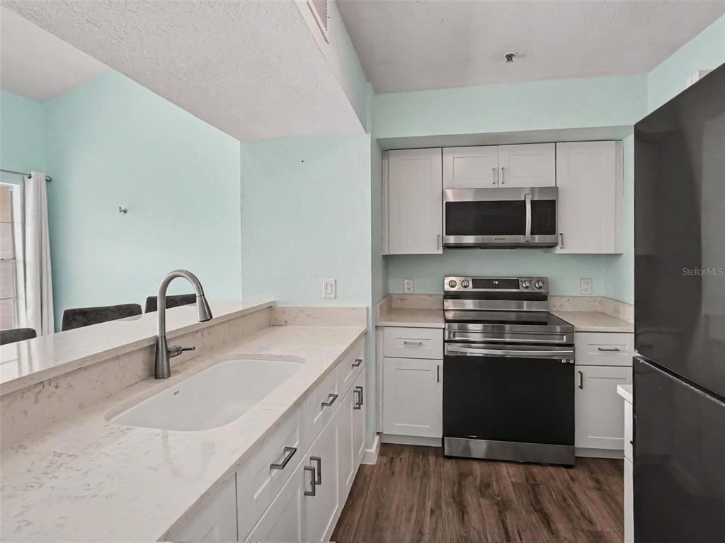 A kitchen features white cabinets, stainless steel appliances, light countertops, and wood-look flooring — 5144 CITY STREET UNIT 233, ORLANDO, FL