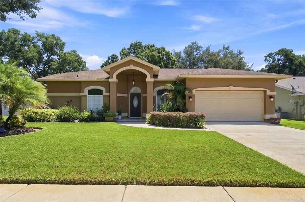 A single-story house with a tan stucco exterior, a two-car garage, and a front lawn — 2244 GROVELAND DRIVE, LUTZ, FL