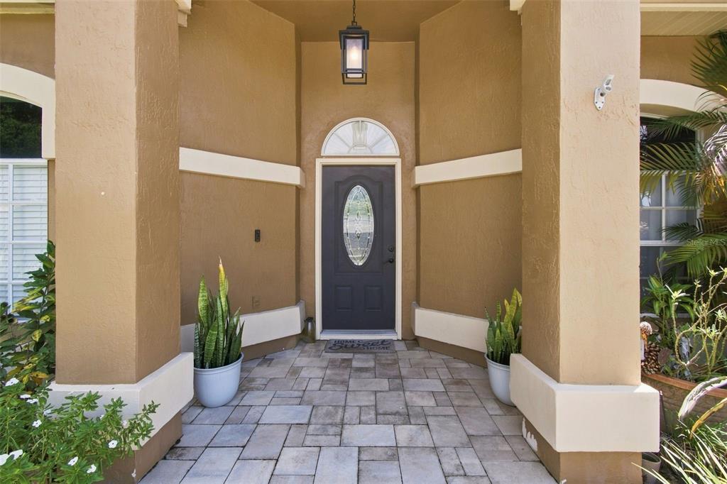 A covered front entryway features a dark gray door, stone pavers, and two potted plants — 2244 GROVELAND DRIVE, LUTZ, FL