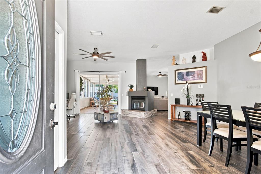 An open-concept living and dining area features wood-look tile flooring and a central fireplace — 2244 GROVELAND DRIVE, LUTZ, FL