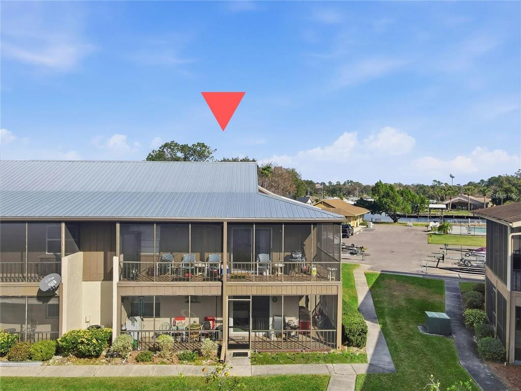 An exterior view of a two-story apartment building with screened-in balconies and a metal roof — 1640 JUNO TRAIL UNIT 204C, ASTOR, FL