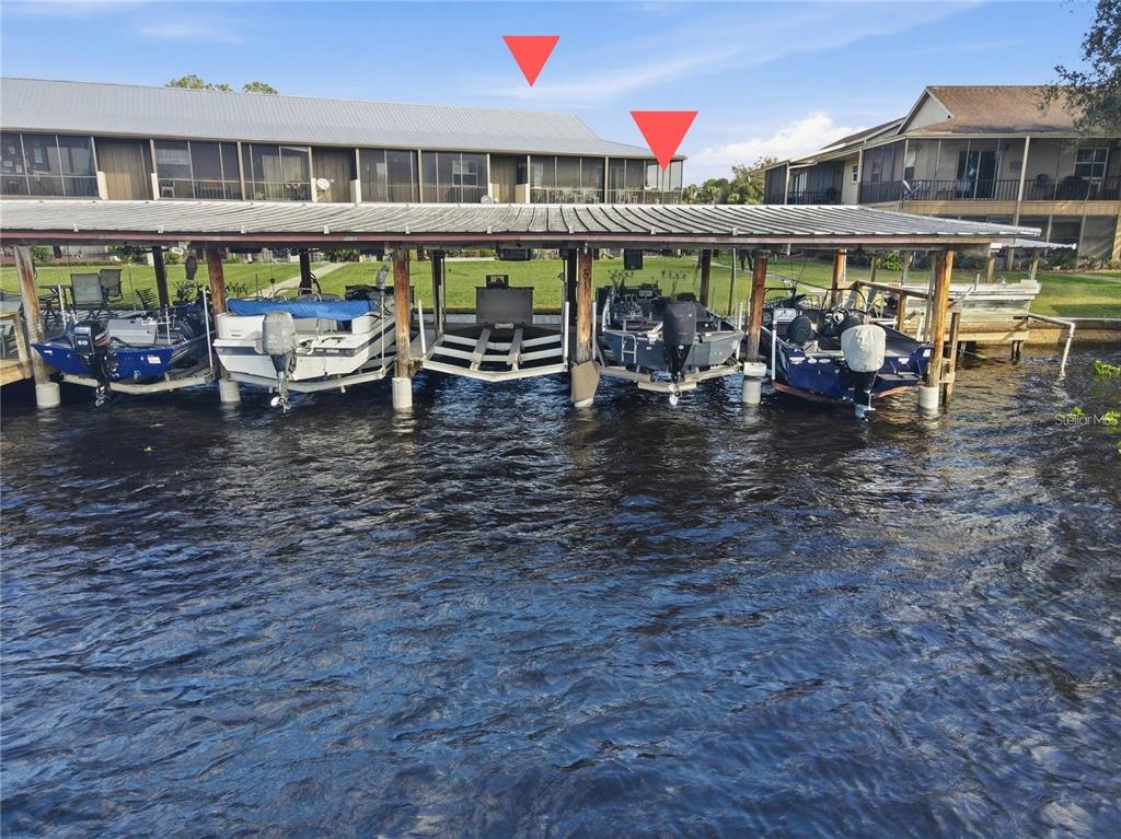 A multi-slip boat dock with several boats sits in front of a waterfront apartment building — 1640 JUNO TRAIL UNIT 204C, ASTOR, FL