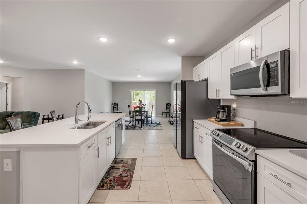 A kitchen with white cabinets, stainless steel appliances, and a large island overlooks a dining area — 703 VOLCO ROAD, EDGEWATER, FL