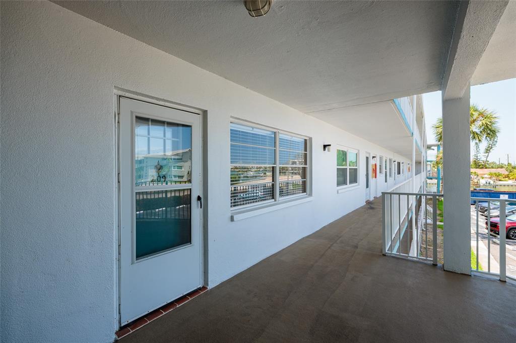 An exterior walkway with white walls, a storm door, and a metal railing — 1893 SHORE DRIVE S UNIT 209, SOUTH PASADENA, FL