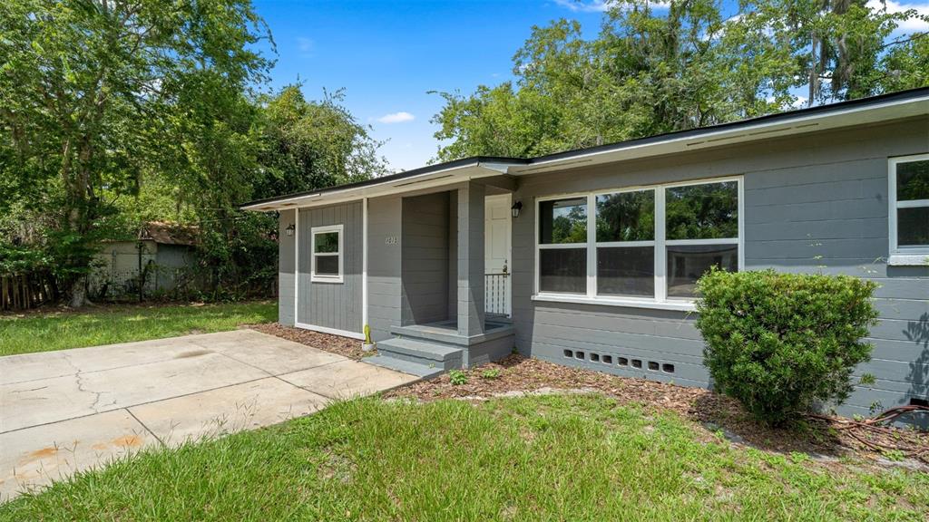 A concrete driveway leads to a grassy yard beside a gray house with two windows — 1015 SE 10TH TERRACE, GAINESVILLE, FL