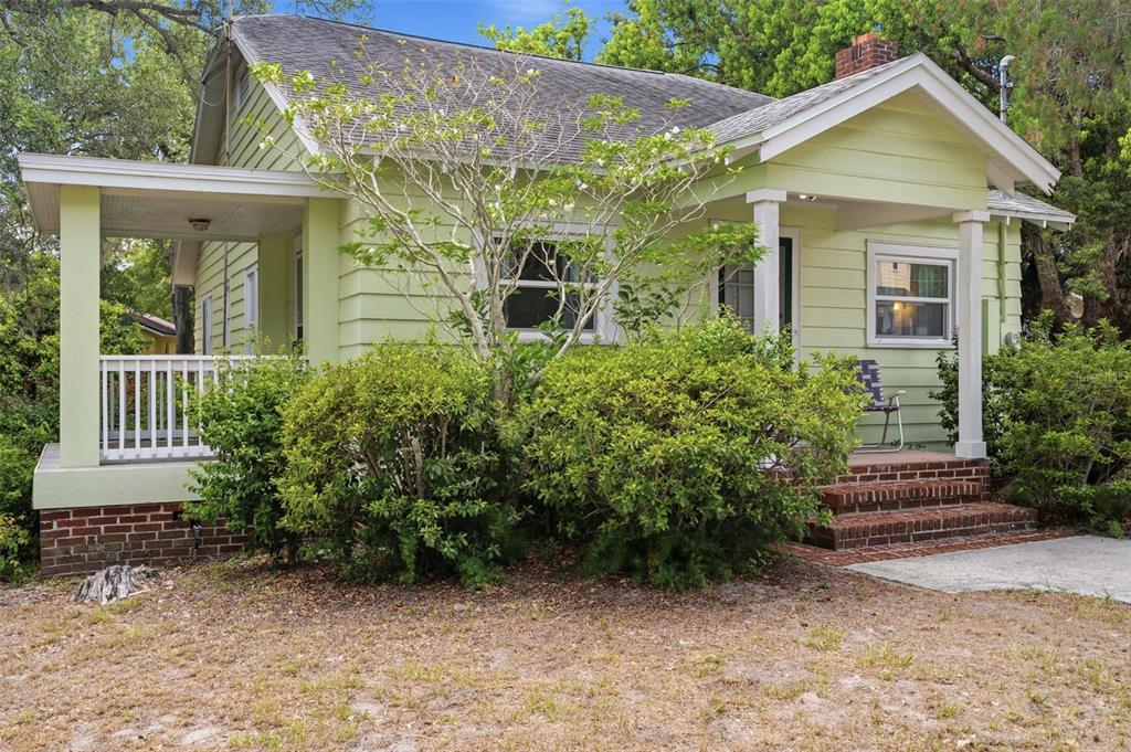 A light green, single-story house features a brick foundation, a front porch, and mature landscaping — 1747 APACHE TRAIL, CLEARWATER, FL