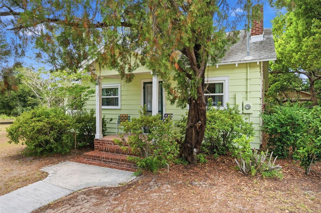 A light green cottage with a brick porch and chimney sits behind a large tree — 1747 APACHE TRAIL, CLEARWATER, FL